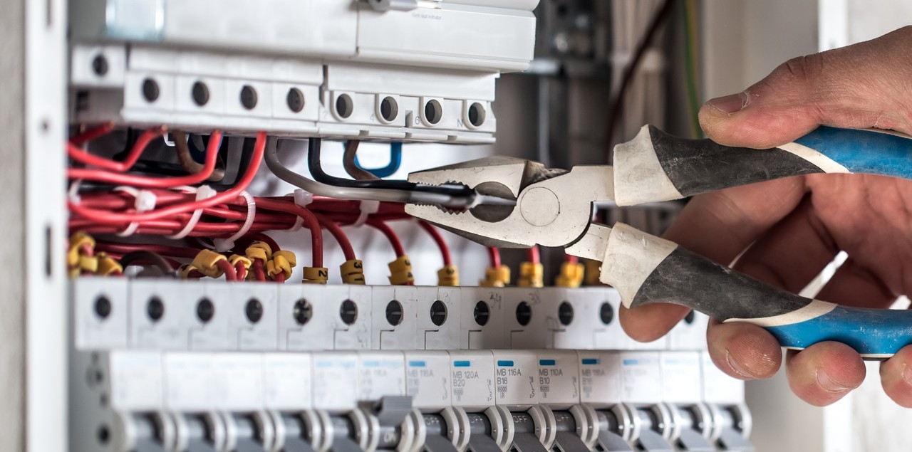 Electrician cu un patent în mână, în fața unui panou electric